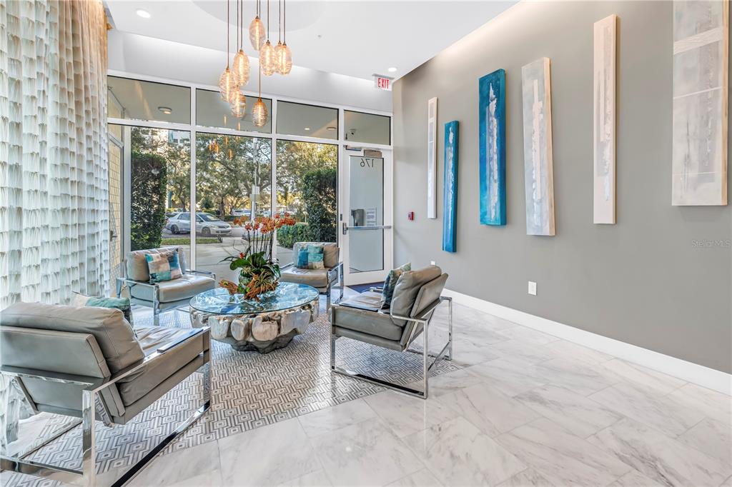 A modern lobby features gray leather armchairs, a glass-topped coffee table, and abstract wall art — 176 4TH AVENUE NE UNIT 1101, ST PETERSBURG, FL