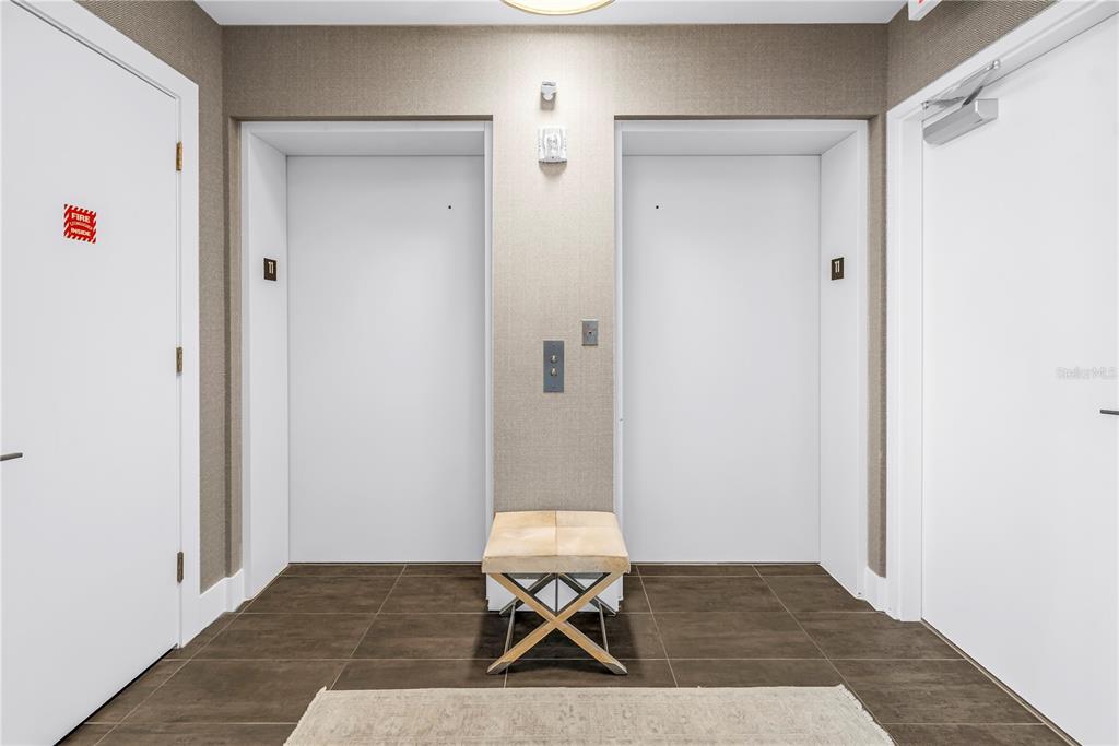An elevator lobby features two white elevator doors, a central bench, and dark tiled flooring — 176 4TH AVENUE NE UNIT 1101, ST PETERSBURG, FL
