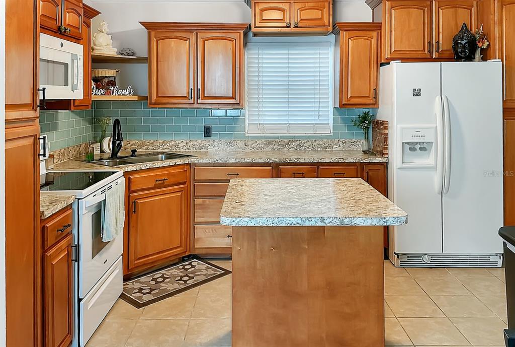 A kitchen with wood cabinets, granite countertops, a center island, and light blue subway tile — 1014 ROOSEVELT AVENUE, BROOKSVILLE, FL