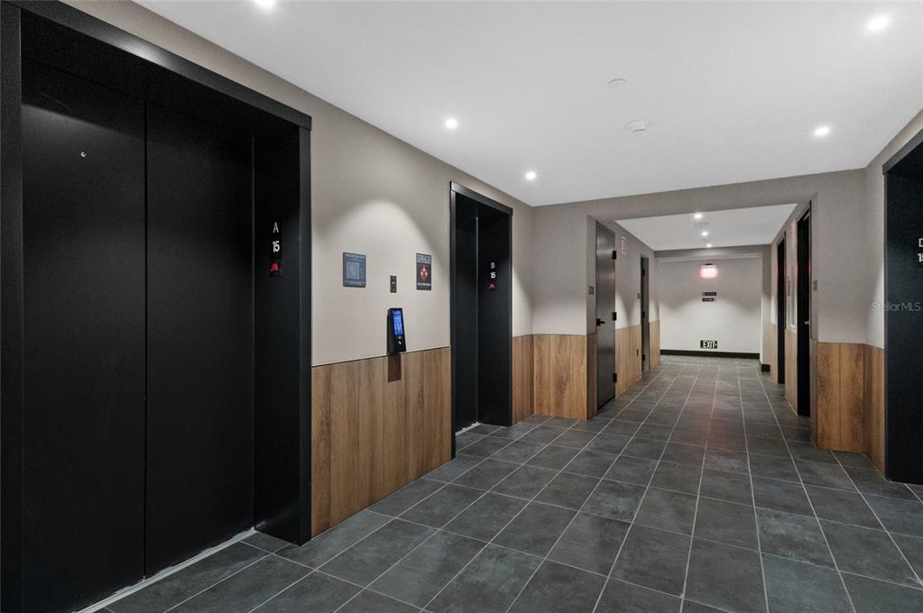 A hallway features two black elevator doors, wood-paneled walls, and dark gray tiled flooring — 121 NE 5TH STREET UNIT 1500, MIAMI, FL