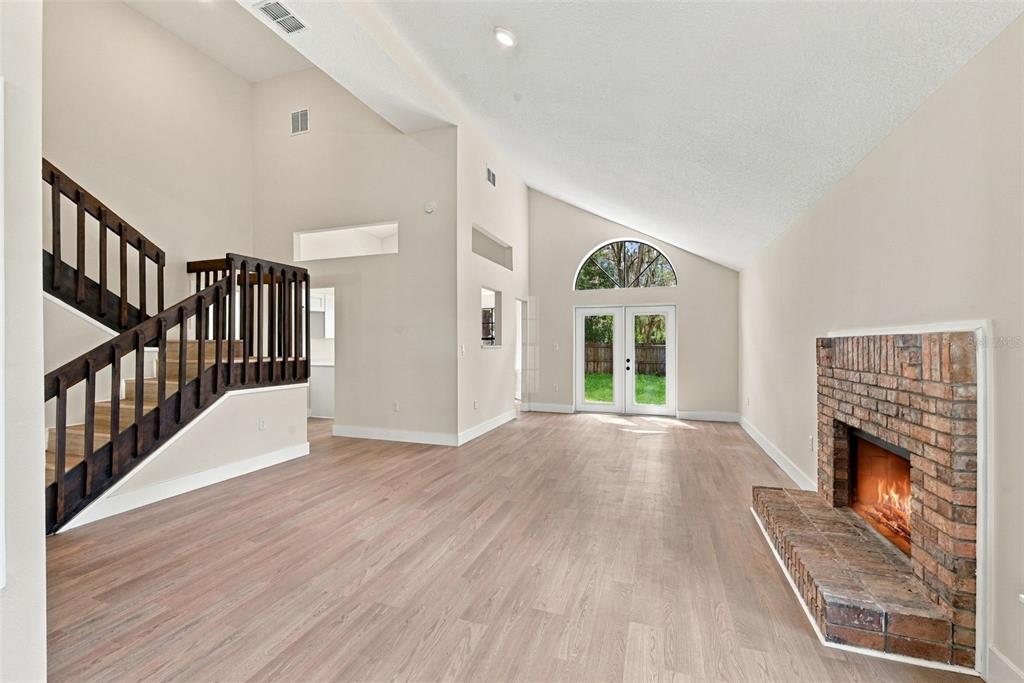 A living room with light wood flooring, a brick fireplace, and a wooden staircase — 2140 WEKIWA OAKS DRIVE, APOPKA, FL