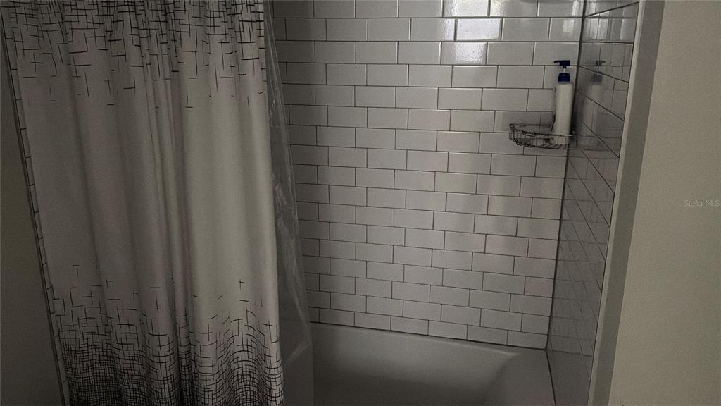 A bathtub with white subway tile walls and a patterned shower curtain — 1804 3RD COURT SE UNIT C, WINTER HAVEN, FL