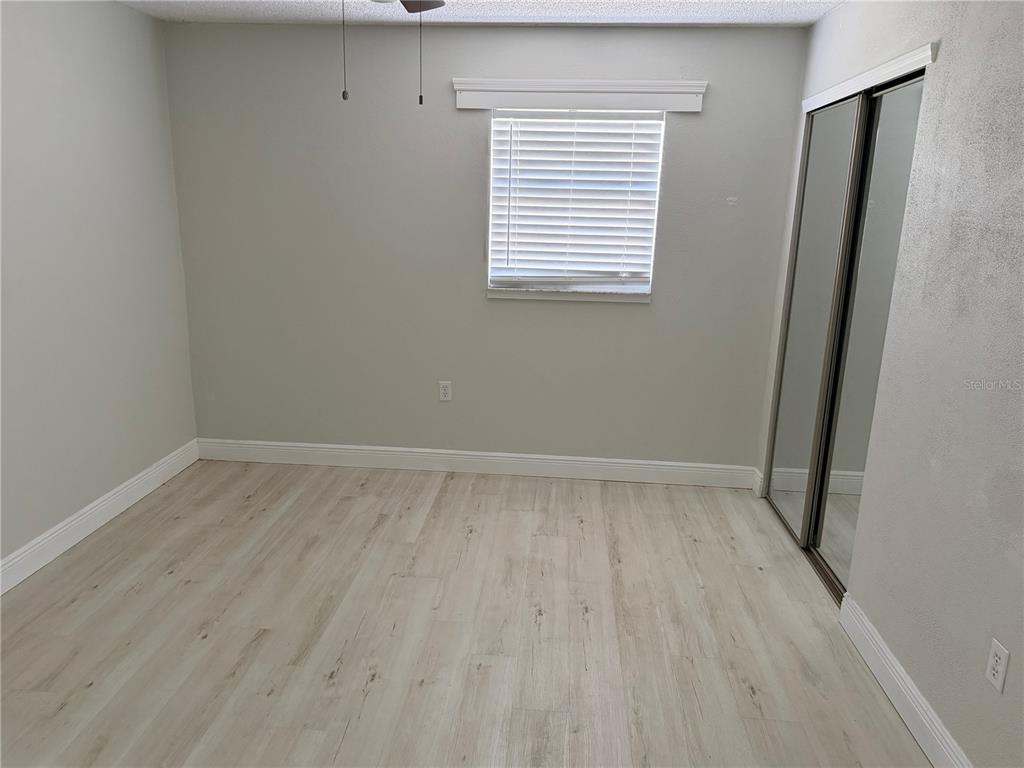 An empty bedroom features light wood-look flooring, gray walls, a window with blinds, and mirrored closet doors — 1804 3RD COURT SE UNIT C, WINTER HAVEN, FL