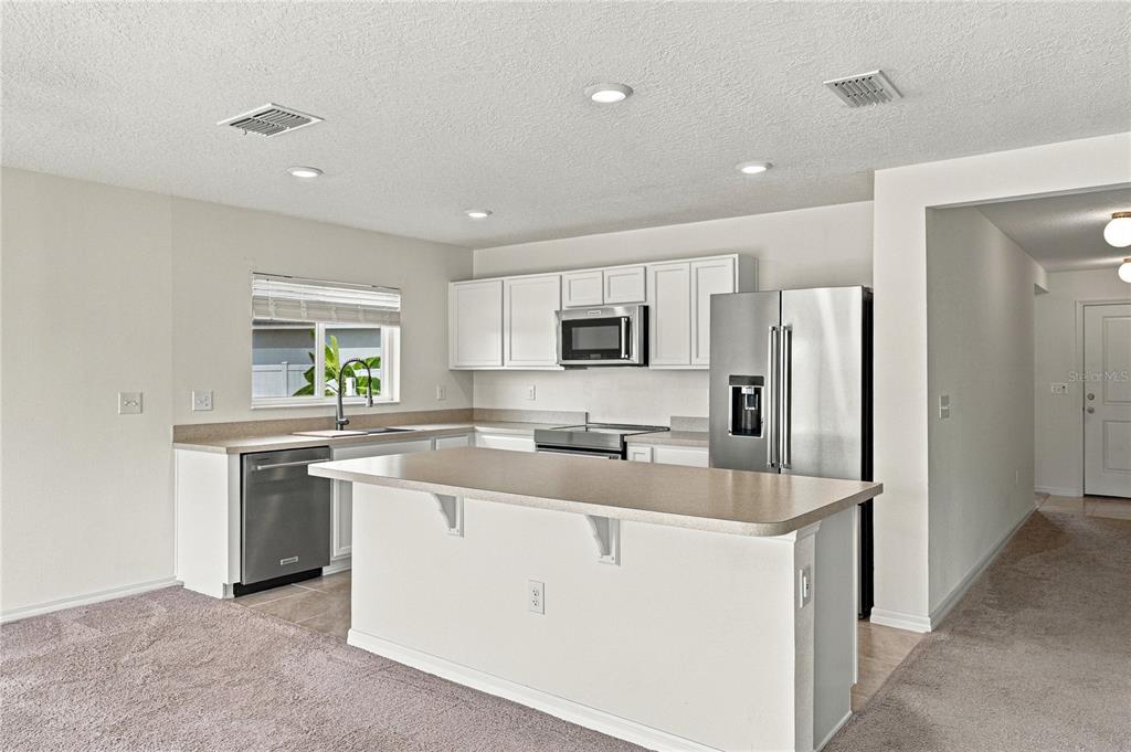 A kitchen with white cabinets, stainless steel appliances, a center island, and beige carpeting — 1444 MATTIE POINTE LANE, AUBURNDALE, FL