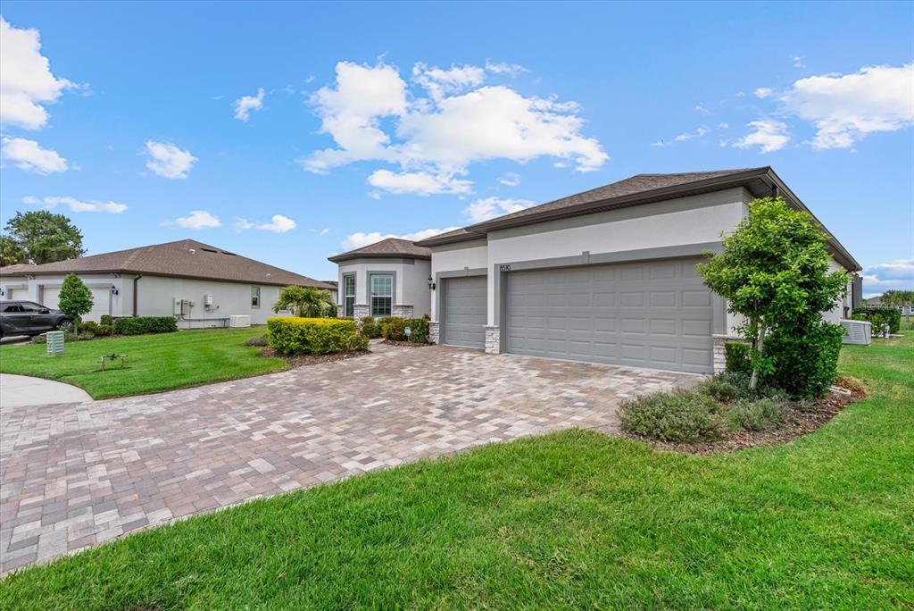 A single-story house with a paver driveway, a three-car garage, and a manicured lawn — 8510 COASTAL PALMS GLEN, PARRISH, FL