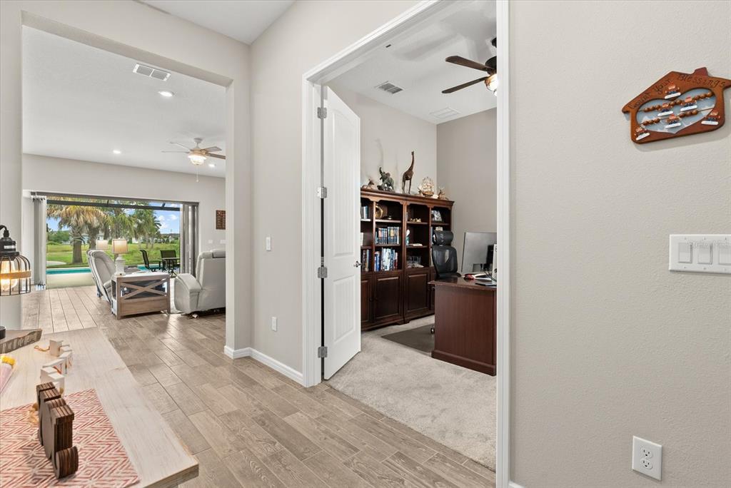 A view from a hallway looking into a home office and an adjacent living area — 8510 COASTAL PALMS GLEN, PARRISH, FL