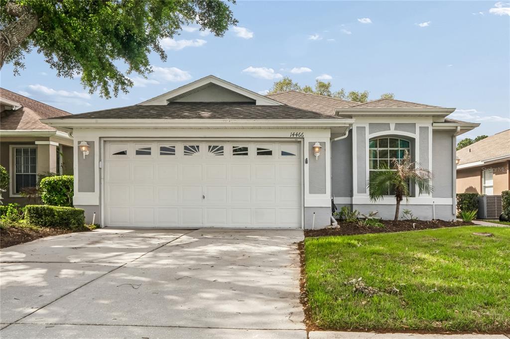 A single-story house with a white two-car garage, gray stucco siding, and a concrete driveway — 14466 TAMARIND LOOP, SPRING HILL, FL