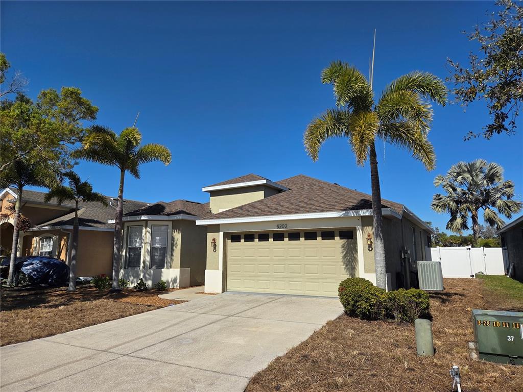 A single-story house with a tan garage, palm trees, and a concrete driveway — 5202 72ND STREET E, PALMETTO, FL