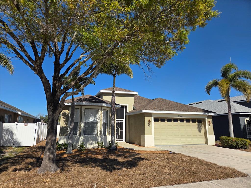 A single-story house with a tan stucco exterior, a two-car garage, and palm trees — 5202 72ND STREET E, PALMETTO, FL