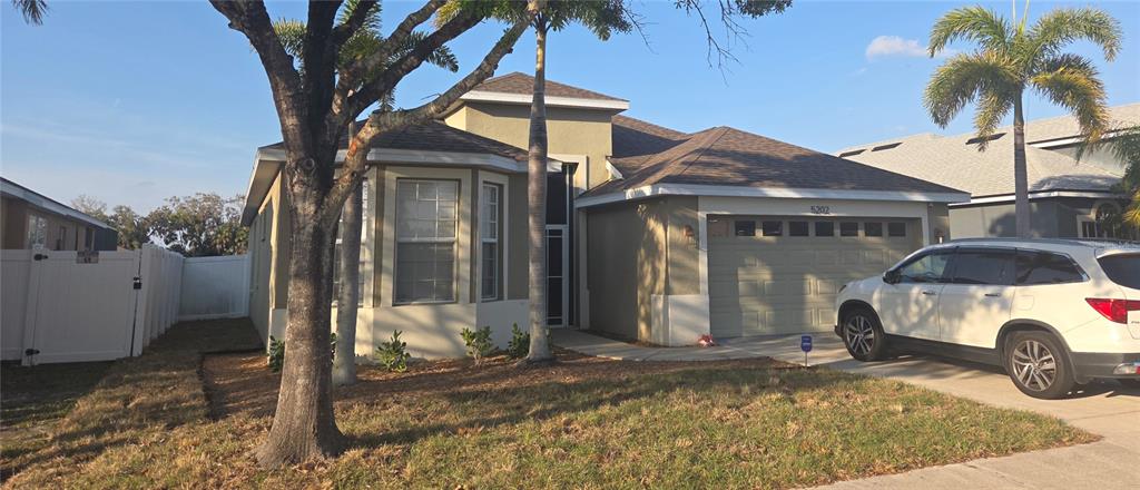 A single-story house with a tan stucco exterior, a two-car garage, and a palm tree — 5202 72ND STREET E, PALMETTO, FL