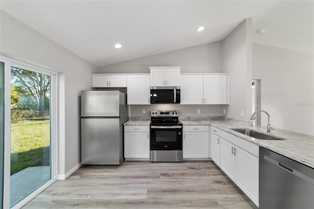 A kitchen with white cabinets, granite countertops, and a stainless steel sink overlooks a dining area — 44 ALMOND ROAD, OCALA, FL