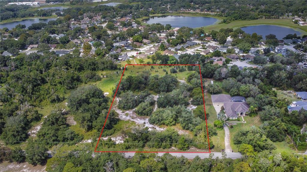 An aerial view shows a vacant, tree-covered rectangular lot outlined in red next to a house — 1156 HIGHLAND ACRES DRIVE, APOPKA, FL