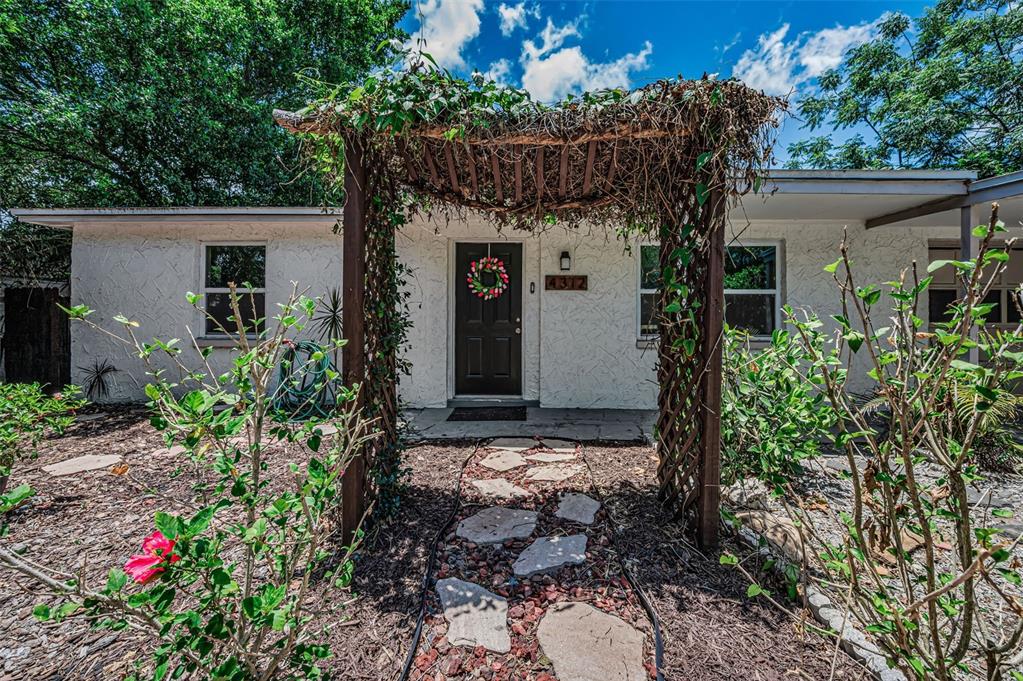 A wooden garden arbor stands over a stone path in a landscaped yard — 4312 BEACON SQUARE DRIVE, HOLIDAY, FL