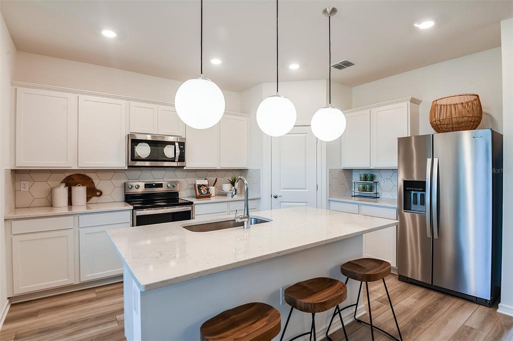A modern kitchen features white cabinets, a quartz-topped island with stools, and stainless steel appliances — 14842 SUNBEAM STREET, PARRISH, FL