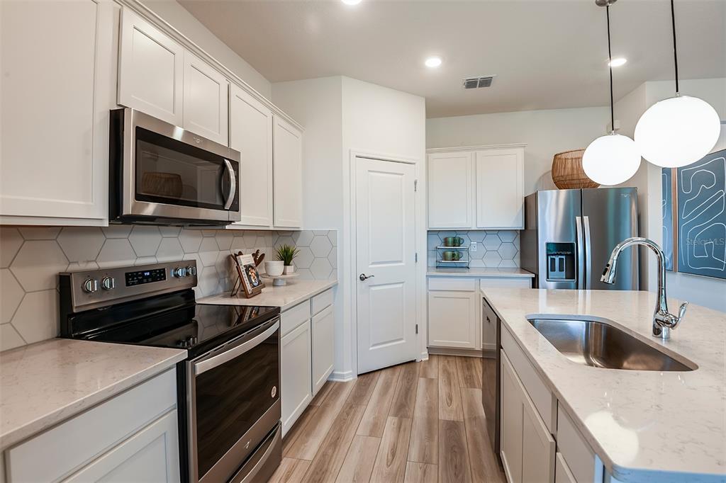 A modern kitchen features white cabinets, stainless steel appliances, quartz countertops, and a hexagonal backsplash — 14842 SUNBEAM STREET, PARRISH, FL
