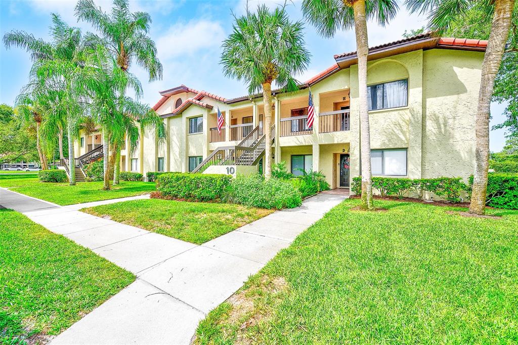 A two-story apartment building with stucco walls, palm trees, and a sidewalk in the foreground — 1801 E LAKE ROAD UNIT 10F, PALM HARBOR, FL