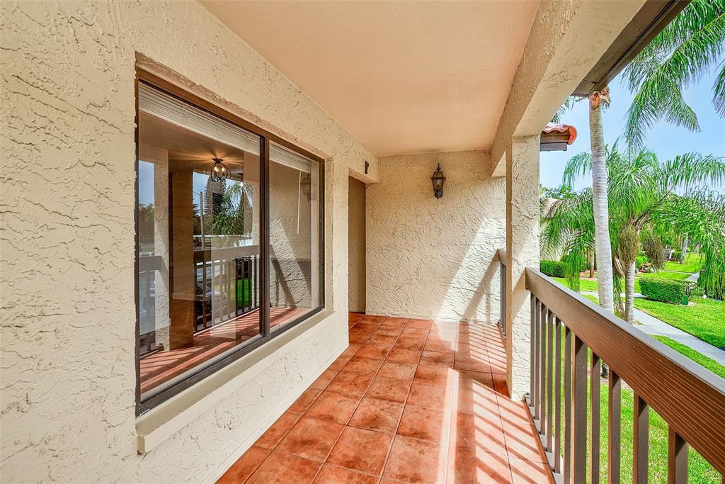 A covered balcony features terracotta tile flooring, a large window, and a wooden railing — 1801 E LAKE ROAD UNIT 10F, PALM HARBOR, FL