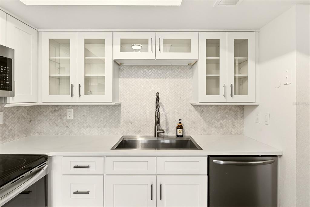 A kitchen features white cabinets, a herringbone tile backsplash, a stainless steel sink, and appliances — 1801 E LAKE ROAD UNIT 10F, PALM HARBOR, FL