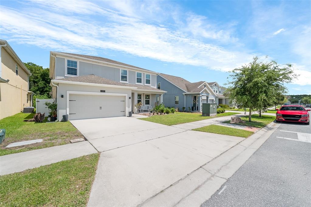 A two-story suburban house with a two-car garage, concrete driveway, and a red car parked nearby — 2353 CRESCENT MOON STREET, KISSIMMEE, FL