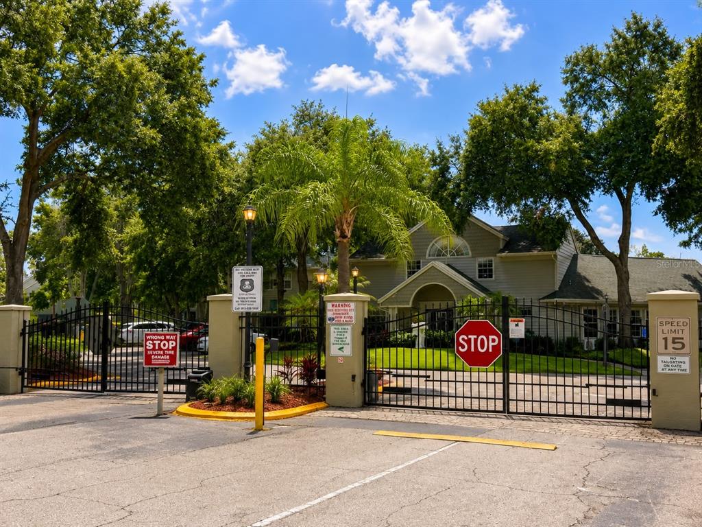 A gated entrance with a metal fence, stop signs, and speed limit sign leads to a building — 5980 WESTGATE DRIVE UNIT 201, ORLANDO, FL