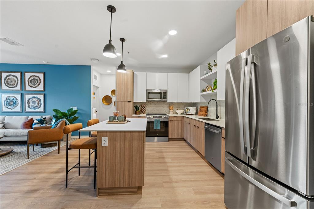A modern kitchen with wood-tone cabinets, stainless steel appliances, and an island with bar seating — 2285 CROWN VILLAGE ROAD UNIT B1.S, OCOEE, FL
