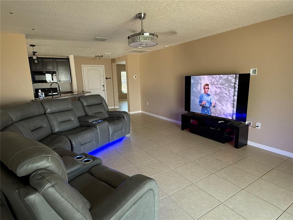 A living room features gray reclining sofas, tile flooring, and a large television on a stand — 820 CHATHAM WALK DRIVE, RUSKIN, FL