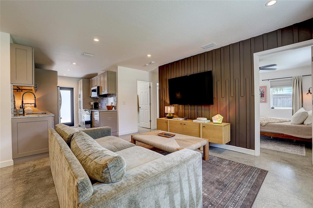 A living room with a gray sofa, wood-paneled accent wall, and an adjacent kitchen area — 2121 PALM TERRACE, SARASOTA, FL