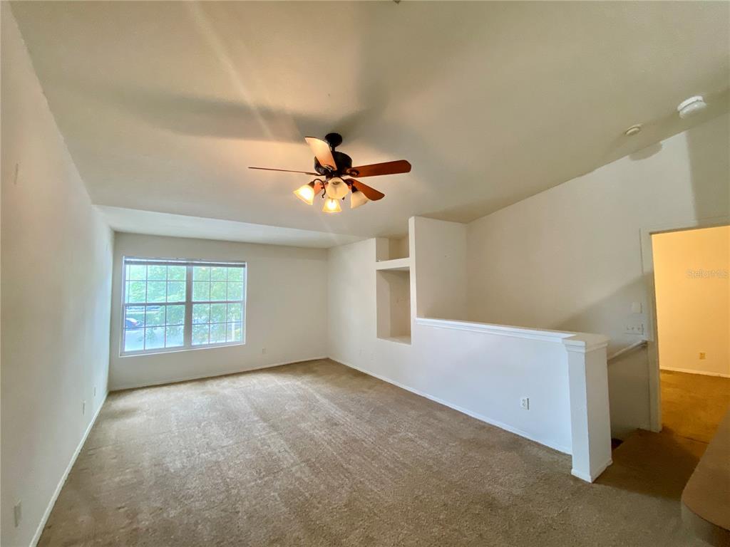 An empty carpeted living room features a ceiling fan, a window, and a half wall — 36101 DEER CREEK DRIVE UNIT 202, ZEPHYRHILLS, FL