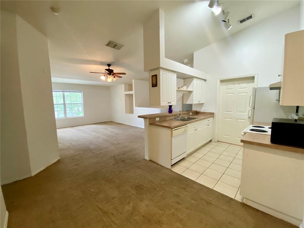 A kitchen with white cabinets and tile floors opens into a carpeted living area — 36101 DEER CREEK DRIVE UNIT 202, ZEPHYRHILLS, FL