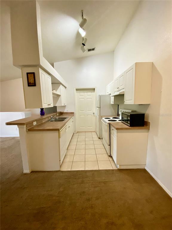 A kitchen with white cabinets, laminate countertops, tile flooring, and a vaulted ceiling — 36101 DEER CREEK DRIVE UNIT 202, ZEPHYRHILLS, FL