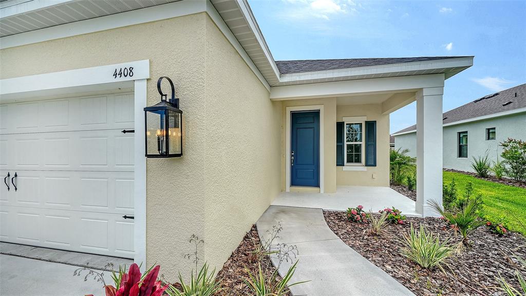 The exterior of a house features a blue front door, a garage, and landscaping — 4408 SPOON BLADE DRIVE, PARRISH, FL