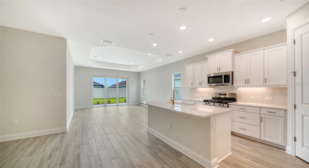 A modern kitchen with white cabinets and an island overlooks an open living area — 4408 SPOON BLADE DRIVE, PARRISH, FL