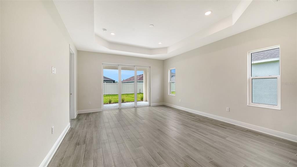An empty room with light-colored walls, gray wood-look flooring, a tray ceiling, and sliding doors — 4408 SPOON BLADE DRIVE, PARRISH, FL