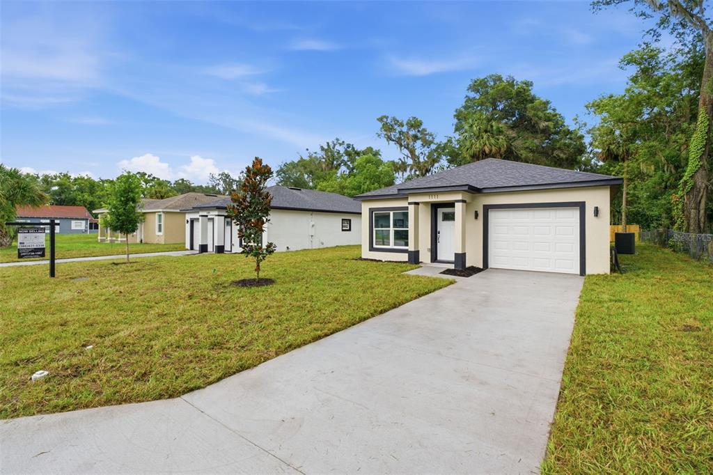 A single-story house with a white garage and beige exterior sits on a grassy lot — 1111 S ADELLE AVENUE, DELAND, FL
