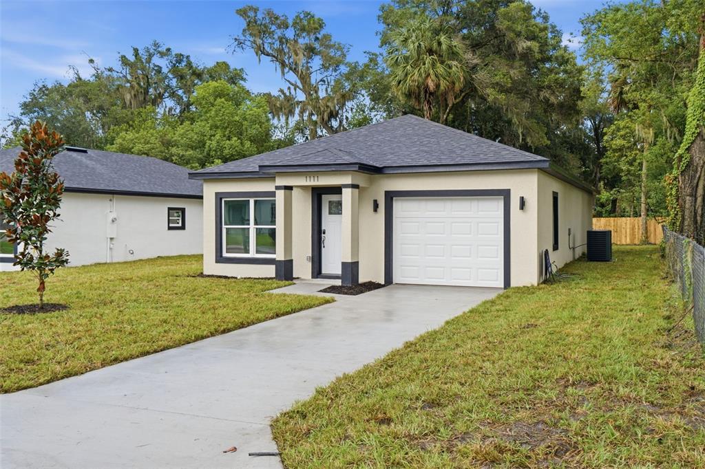 A single-story house with a concrete driveway, a one-car garage, and a light-colored stucco exterior — 1111 S ADELLE AVENUE, DELAND, FL