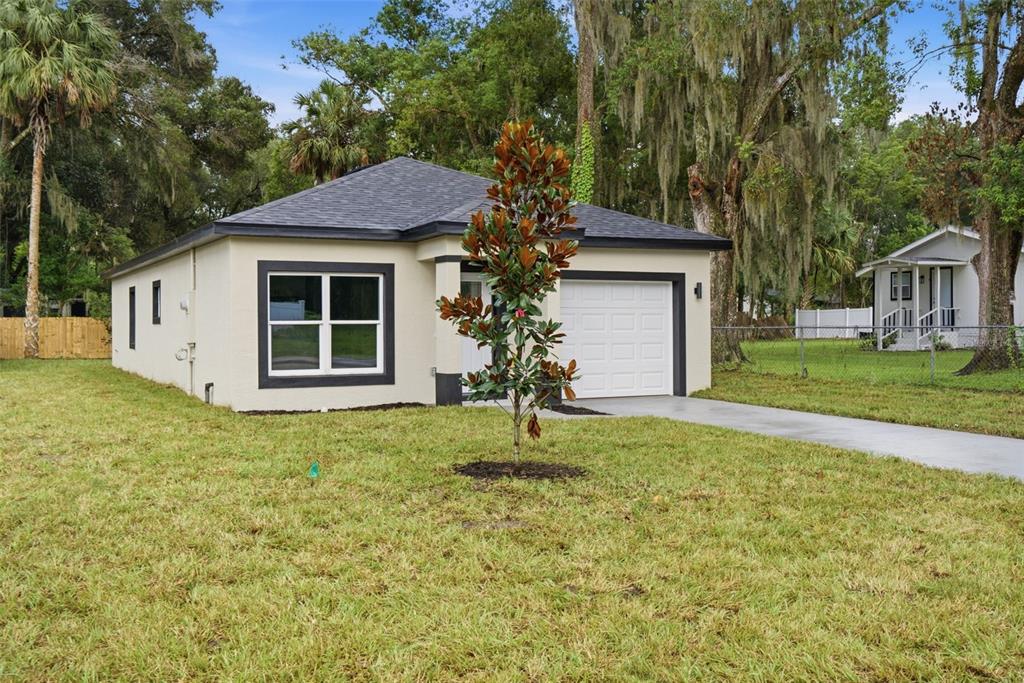 A single-story house with a white exterior, dark trim, and a small tree in front — 1111 S ADELLE AVENUE, DELAND, FL