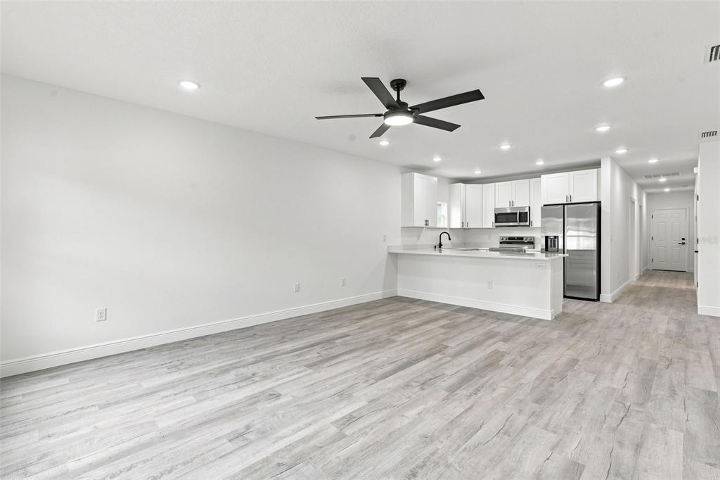 A bright, open-concept living area with light wood-look flooring and a modern kitchen — 1111 S ADELLE AVENUE, DELAND, FL