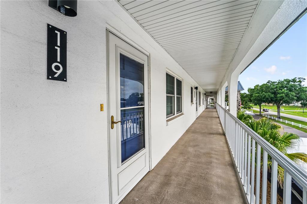 A dining area with a square table and chairs sits adjacent to a carpeted living room — 4801 AIRPORT ROAD UNIT 119, ZEPHYRHILLS, FL