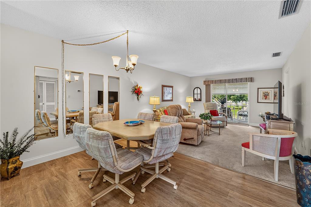 A living room with beige carpet, a floral sofa, two recliners, and an adjacent dining area — 4801 AIRPORT ROAD UNIT 119, ZEPHYRHILLS, FL