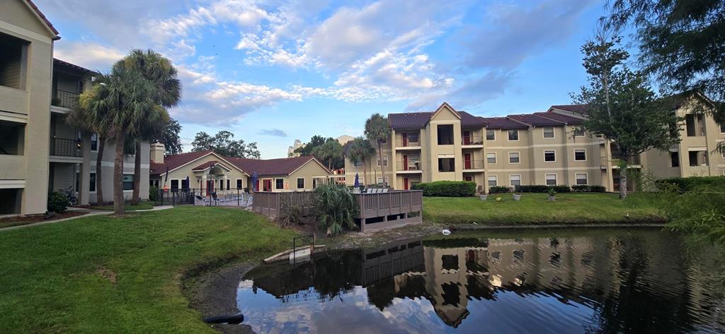 Exterior view of apartment buildings with a pond, pool area, and palm trees — 3004 PARKWAY BOULEVARD UNIT 210, KISSIMMEE, FL