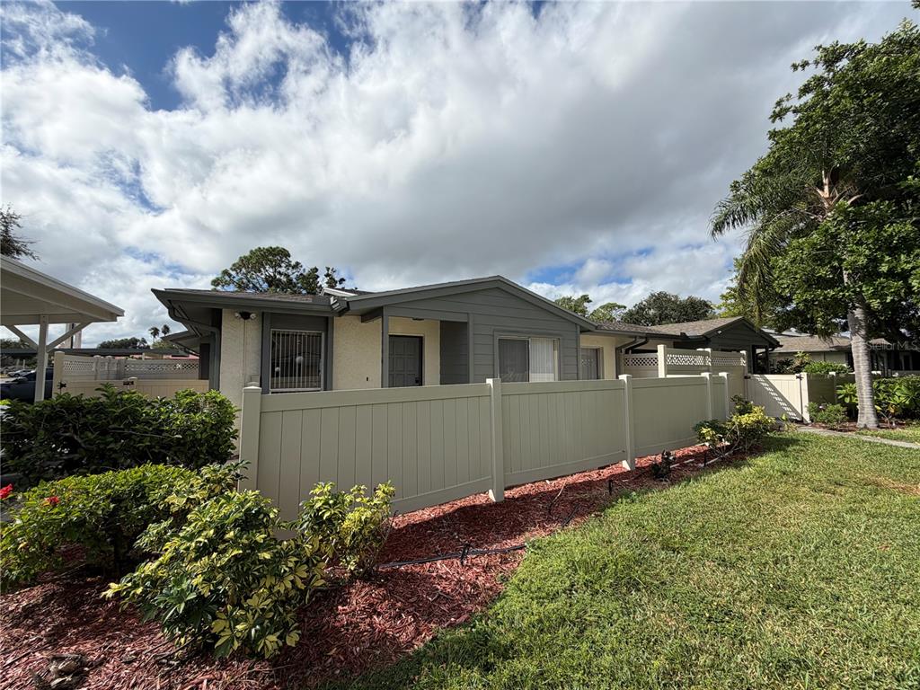 A single-story house exterior features a tan fence, gray trim, and a landscaped yard — 2606 29TH AVE W UNIT 12, BRADENTON, FL