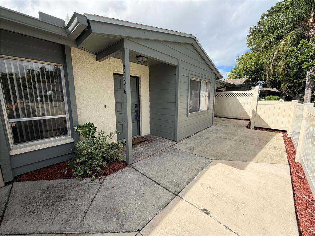The exterior of a house features a gray door, concrete walkway, and white privacy fencing — 2606 29TH AVE W UNIT 12, BRADENTON, FL