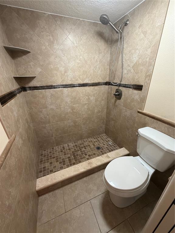 A bathroom featuring a tiled walk-in shower with a handheld sprayer and a white toilet — 2606 29TH AVE W UNIT 12, BRADENTON, FL