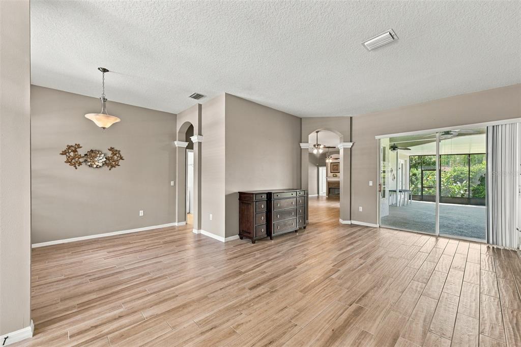 A living room features light wood-look tile flooring, red armchairs, and a beige sofa — 7521 MELOGOLD CIRCLE, LAND O LAKES, FL