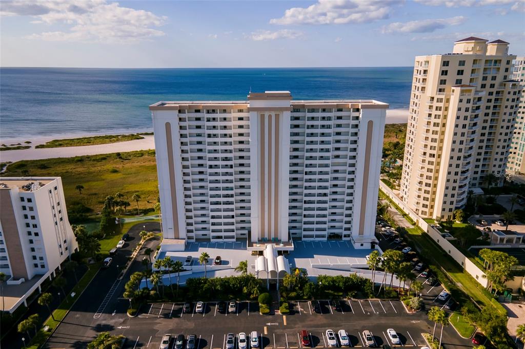 A living room features two beige sofas, a glass-topped coffee table, and large windows — 1230 GULF BOULEVARD UNIT 306, CLEARWATER BEACH, FL