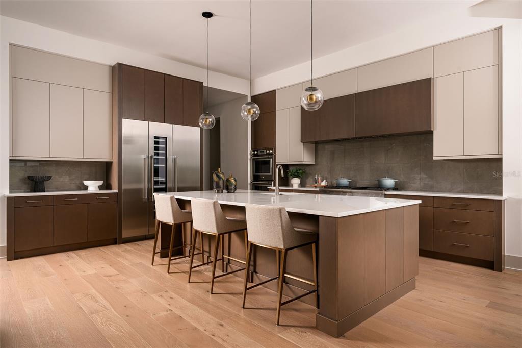 A modern kitchen features two-toned cabinetry, a large white island with barstools, and wood flooring — 8613 SANDPOINT STREET, SARASOTA, FL
