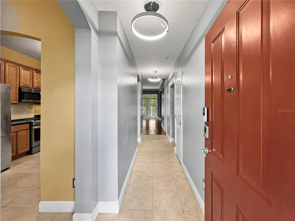 A hallway with tile flooring leads from a red front door toward a back entrance — 1411 CELEBRATION AVENUE UNIT 206, CELEBRATION, FL