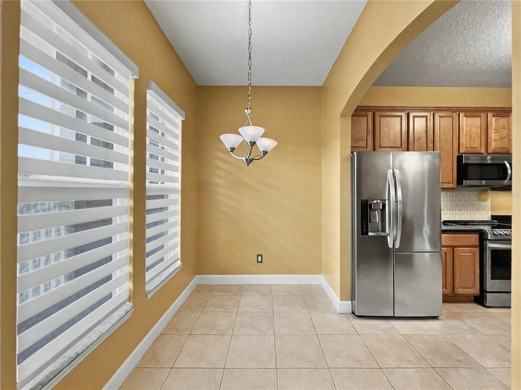 A dining area features tile flooring, a chandelier, two windows with blinds, and a kitchen — 1411 CELEBRATION AVENUE UNIT 206, CELEBRATION, FL