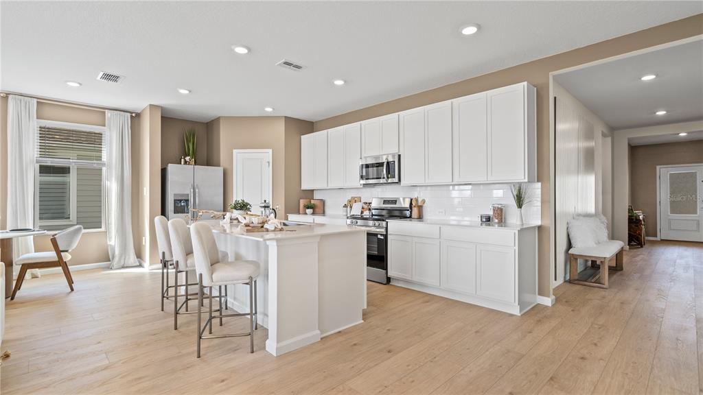A modern kitchen features white cabinetry, a large island with bar seating, and light wood flooring — 2866 PIONEER TRAIL, EAGLE LAKE, FL