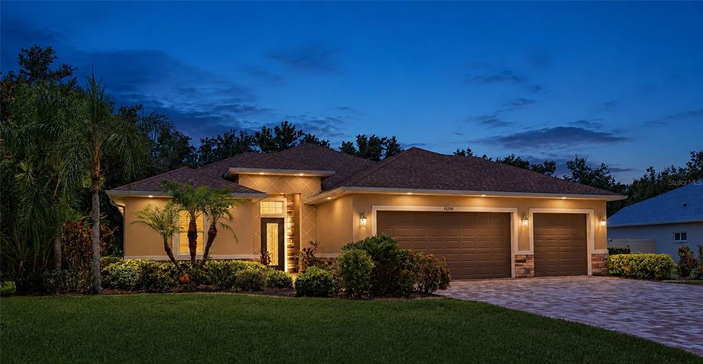 A single-story house with a three-car garage and a paved driveway at dusk — 15208 21ST AVENUE E, BRADENTON, FL